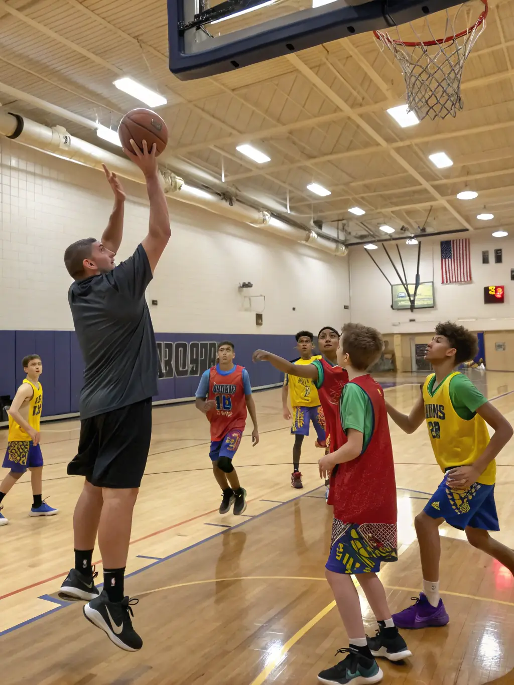 Teenagers are participating in a basketball training session indoors, with a coach demonstrating techniques and strategies.